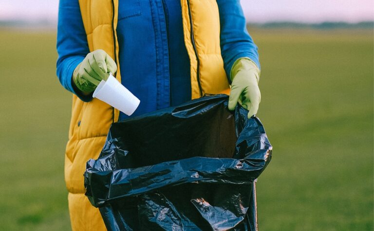 A volunteer putting a plastic piece of trash in a bag during a volunteer cleanup event